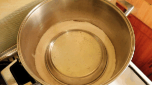No-oven sourdough bread baking setup with salt spread at the bottom of a deep pan and a metal plate placed on top as a trivet.